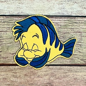 May include: Embroidered patch featuring a cartoon fish with a yellow body and blue fins and hair. The fish is smiling with its eyes closed and its hands covering its mouth. The patch has a black outline.