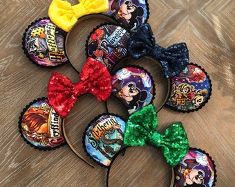 May include: Four pairs of Harry Potter themed Minnie Mouse ears with different house crests. The ears are black with a black headband and a bow. The bows are yellow, red, green, and blue. The crests are Gryffindor, Slytherin, Hufflepuff, and Ravenclaw.