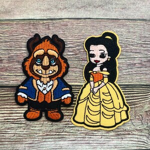 May include: Two embroidered patches featuring characters from a fairy tale. One patch depicts a cartoon version of a beast in orange, brown, blue, and black. The other patch shows a princess in a yellow dress with black hair.