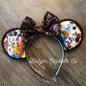 May include: A pair of brown and white mouse ears with a brown sequined bow. The ears feature a Thanksgiving-themed print with Mickey Mouse, Minnie Mouse, Pluto, and Stitch. The headband is black and white. The text "Kadyrn Elizabeth Co." is printed on the headband.