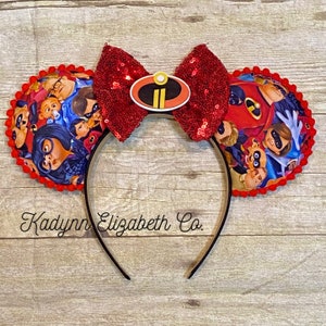 May include: Red sequined Minnie Mouse ears with a black headband. The ears are decorated with a print of the Incredibles family and a red bow with a black and yellow Incredibles logo.