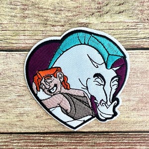 May include: Embroidered patch featuring Hercules embracing Pegasus, set against a heart-shaped backdrop. Hercules has orange hair and is wearing a brown tunic. Pegasus is white with a teal mane. The patch has a black border.