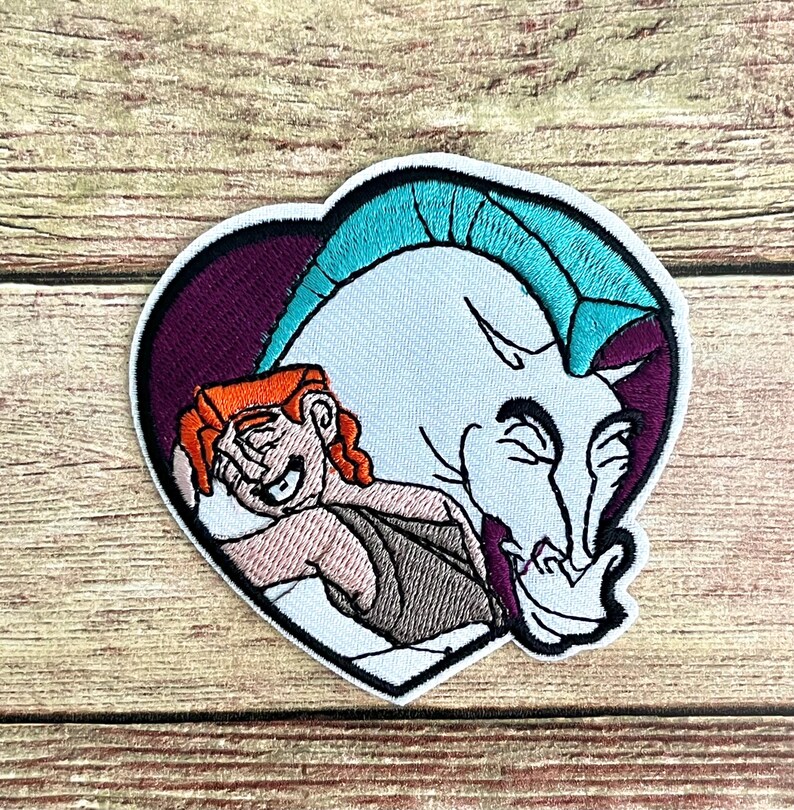 May include: Embroidered patch featuring Hercules embracing Pegasus, set against a heart-shaped backdrop. Hercules has orange hair and is wearing a brown tunic. Pegasus is white with a teal mane. The patch has a black border.