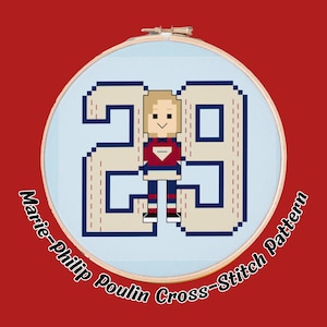 May include: A cross-stitch pattern featuring the number 29 and a pixelated figure in a hockey uniform. The design is set within a round embroidery hoop against a red background. The text "Marie-Philip Poulin Cross-Stitch Pattern" is curved around the hoop.