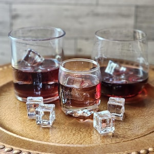 May include: Three clear glass cups filled with a dark red liquid and ice cubes on a wooden tray. The tray has a gold rim and a beaded edge.