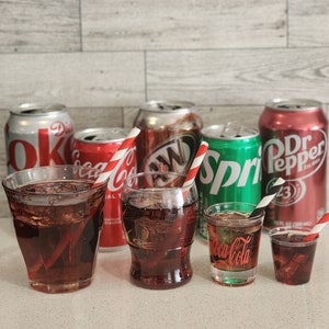 May include: A selection of soda cans and glasses filled with cola, including Dr Pepper, Sprite, and Coca-Cola. The glasses have red and white striped straws.