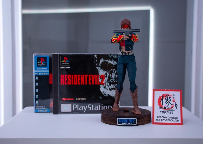 Puede incluir: Una figura de acci&oacute;n roja y negra de una mujer sosteniendo una pistola, de pie sobre una base con las palabras "Resident Evil 2" impresas en ella. La figura es del videojuego Resident Evil 2, y la base es un expositor. La figura lleva una chaqueta roja y negra con un dise&ntilde;o de llamas, pantalones vaqueros azules y botas negras. La figura sostiene una pistola en su mano derecha y la apunta a la c&aacute;mara. La figura est&aacute; de pie sobre una base que est&aacute; hecha de madera y tiene una base negra. La base tiene las palabras "Resident Evil 2" impresas en ella en letras blancas. La figura es del videojuego Resident Evil 2, que fue lanzado para PlayStation en 1998.