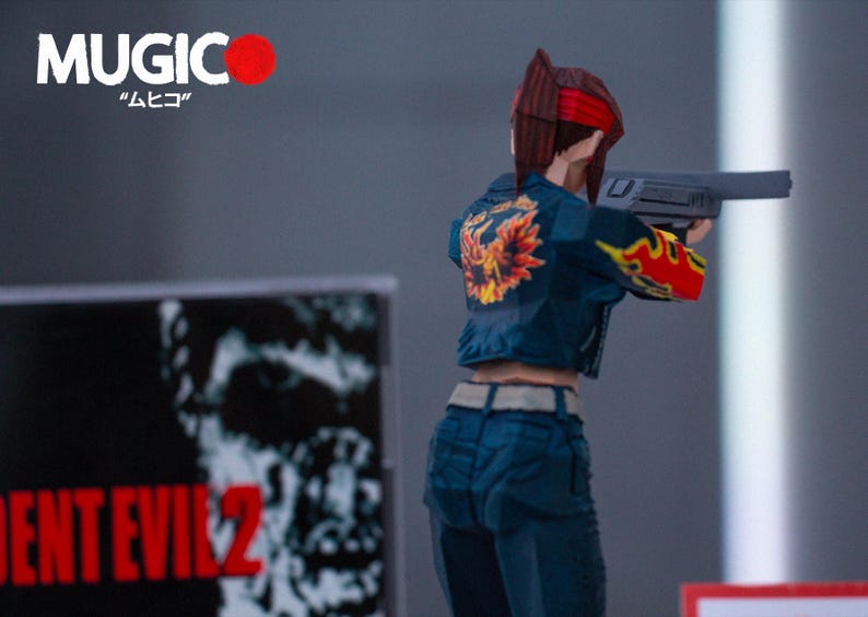 Puede incluir: Una figura de acci&oacute;n azul y roja de una mujer sosteniendo una pistola. La figura lleva una chaqueta vaquera azul con un dise&ntilde;o de llamas amarillas y naranjas en la espalda. La figura est&aacute; de pie frente a una caja en blanco y negro con el texto "Resident Evil 2" en ella.