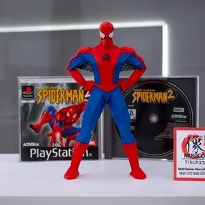 May include: A red and blue Spider-Man action figure stands in front of two PlayStation game cases. The figure has its arms on its hips. The game cases are for Spider-Man and Spider-Man 2. A small red card with Japanese text is on the right.