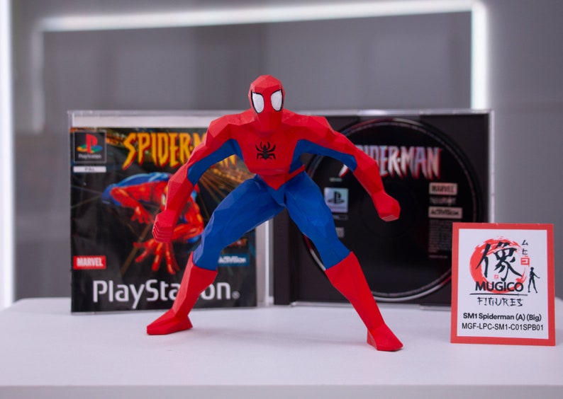 May include: A red and blue Spiderman action figure in a dynamic pose, standing in front of two Playstation game cases. The figure is made of a low-poly style, with a black spider logo on the chest. The game cases are for the Spiderman game for the Playstation console.