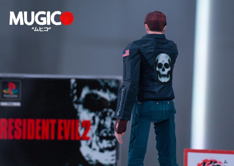 May include: A black and white action figure of a man wearing a black leather jacket with a white skull on the back. The figure is standing in front of a video game case for Resident Evil 2.