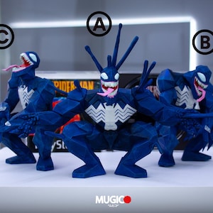 May include: Three blue Venom figures with white chest emblems and open mouths displaying pink tongues and sharp teeth. The figures are in a crouching position. The figures are on a white surface.