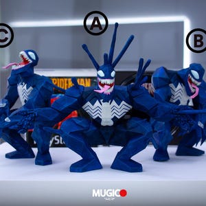 Puede incluir: Tres figuras azules de Venom con emblemas blancos en el pecho y bocas abiertas que muestran lenguas rosas y dientes afilados. Las figuras est&aacute;n en posici&oacute;n de cuclillas. Las figuras est&aacute;n sobre una superficie blanca.