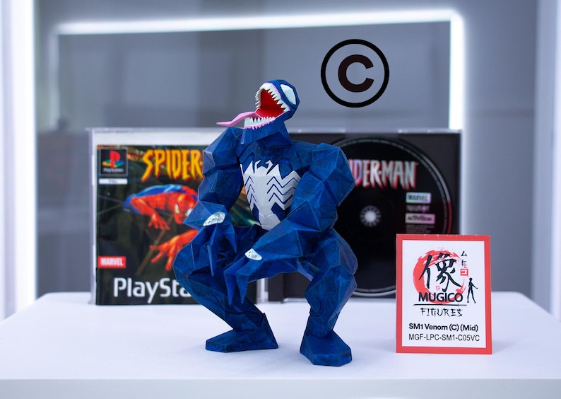 Puede incluir: Una figura azul de Venom con un emblema de ara&ntilde;a blanco, boca abierta y lengua larga, posando frente a una caja de juego de PlayStation de Spider-Man y una caja de CD. Una peque&ntilde;a tarjeta dice "MUGICO FIGURES".
