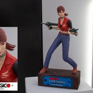 Könnte beinhalten: Eine rote und blaue Actionfigur einer Frau, die eine Waffe hält. Die Figur steht auf einem Holzsockel mit einer blauen Plakette, auf der "Resident Evil CODE: Veronica Claire Redfield" steht.