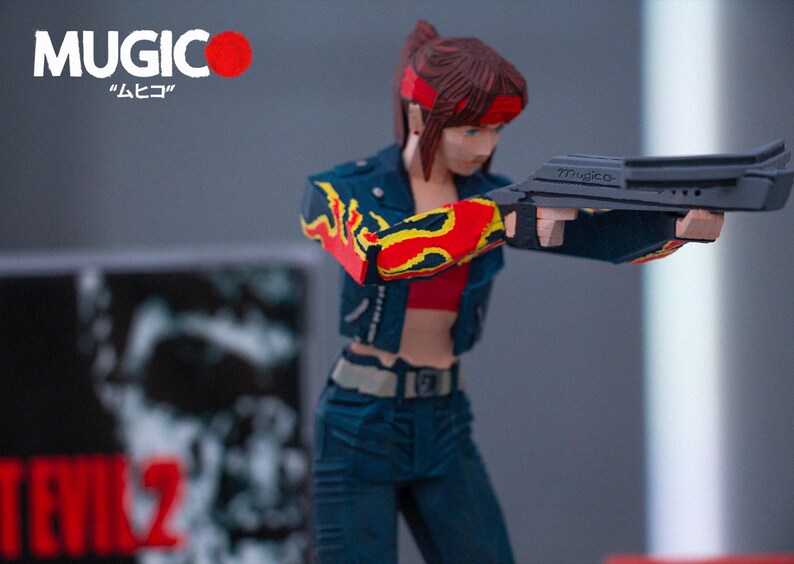 Puede incluir: Una figura de acci&oacute;n de pelo rojo que lleva una chaqueta vaquera azul con llamas amarillas y rojas en las mangas, un top rojo y unos vaqueros azules. La figura sostiene una pistola negra con la palabra "MUGICO" impresa en ella. La figura est&aacute; de pie sobre una superficie gris.