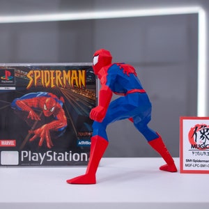 May include: A red and blue Spider-Man action figure in a crouching pose. The figure is made of a polygon style material. The figure is standing next to a PlayStation game case for Spider-Man. The game case has a red and blue Spider-Man on the cover. A small red card with Japanese text and the words "MUGICO FIGURES" is in the foreground. The card also has the text "SM1 Spiderman (A) (Big) MGF-LPC-SM1-C01SPB01".