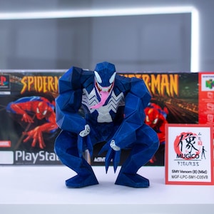 May include: A blue Venom figure with a white spider emblem and a pink tongue, posed in front of a Spider-Man PlayStation game box and a red Nintendo 64 box. A small red card with Japanese text is also present.