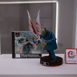 May include: A figure of a zombie-like character with large, bloody wings, a blue coat, and green skin. A PlayStation game case with the title "Clock Tower" is behind the figure. A small sign with Japanese text is to the right.
