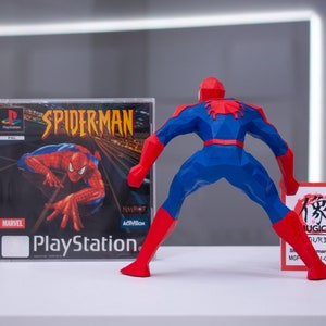 May include: A red and blue 3D printed figurine of Spider-Man standing with his back to the camera. The figurine is holding a small card with Japanese text that reads "Mugico Figures" and "Spider-Man (A) (Big)". The figurine is next to a PlayStation game case for Spider-Man.