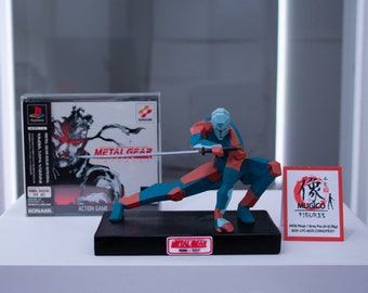 May include: A blue, red, and white polygonal figurine of a character from the Metal Gear video game series. The figurine is holding a sword and is posed in a crouching position. The figurine is on a black base with a Metal Gear logo. The figurine is next to a PlayStation game case for Metal Gear Solid. The case is in Japanese. There is a red card with Japanese text and the words "MUGICO FIGURES" on it.