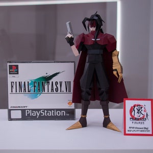May include: A red and black papercraft figure of Vincent Valentine from Final Fantasy VII, holding a gun. The figure is standing on a white surface in front of a PlayStation game case for Final Fantasy VII. A red and white sign with Japanese text and the words "MUGI FIGURES" is in the foreground. The sign also includes the text "FFVII Vincent (Big) MGF-LPC-FF7-809V21001".