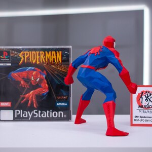 May include: A red and blue 3D printed figurine of Spiderman, standing with one leg forward and holding a red and white card with Japanese text and the words "MUGICO FIGURES" and "SM1 Spiderman (A) (Big) MGF-LPC-SM1-C015PB01". The figurine is next to a Playstation game case for Spiderman.