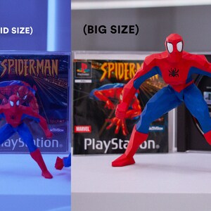 May include: Two different sized red and blue Spider-Man figurines standing in front of PlayStation game cases. The game cases have the text "Spider-Man" on them.