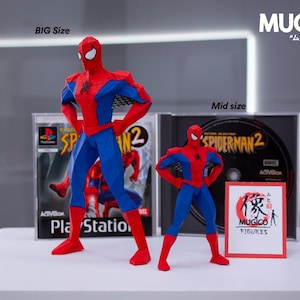 May include: Two Spider-Man action figures, one large and one mid-size, stand in front of PlayStation and DVD cases for Spider-Man 2. The figures are red and blue, with white eye masks. The text "BIG Size" and "Mid size" are visible.