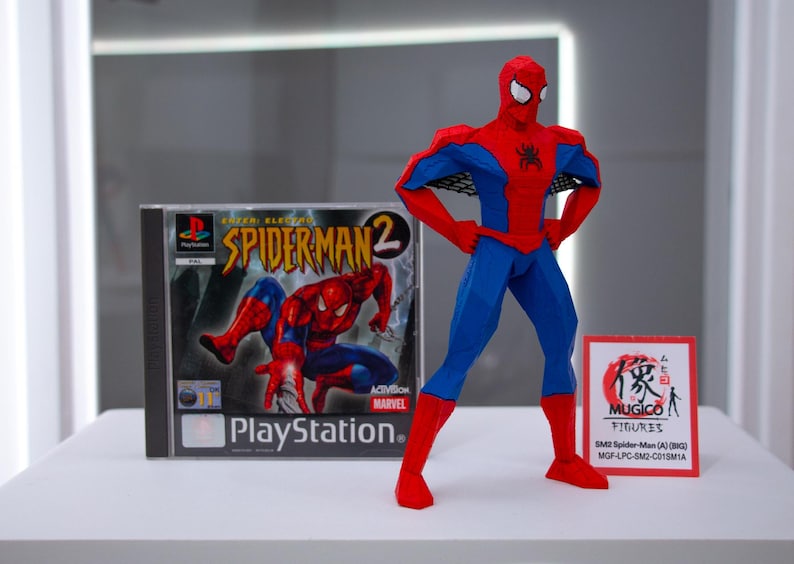 May include: A red and blue Spider-Man figure stands next to a PlayStation game case for Spider-Man 2. The figure has a geometric design. A small sign with Japanese text is also present.