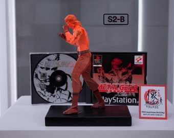 May include: A red and orange figurine of a character from the video game Metal Gear Solid. The figurine is posed in a fighting stance. The figurine is on a black base and is accompanied by a Metal Gear Solid video game case and a small card with the text "MUGICO FIGURES MGS Liquid Snake (SD-01) Big MOF-LPCMGS-C520501".