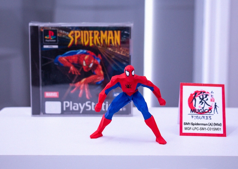 May include: A red, blue, and black Spider-Man action figure stands before a PlayStation game case. The game case features the title "SPIDERMAN" and the Marvel logo. A small card with Japanese text is also present.