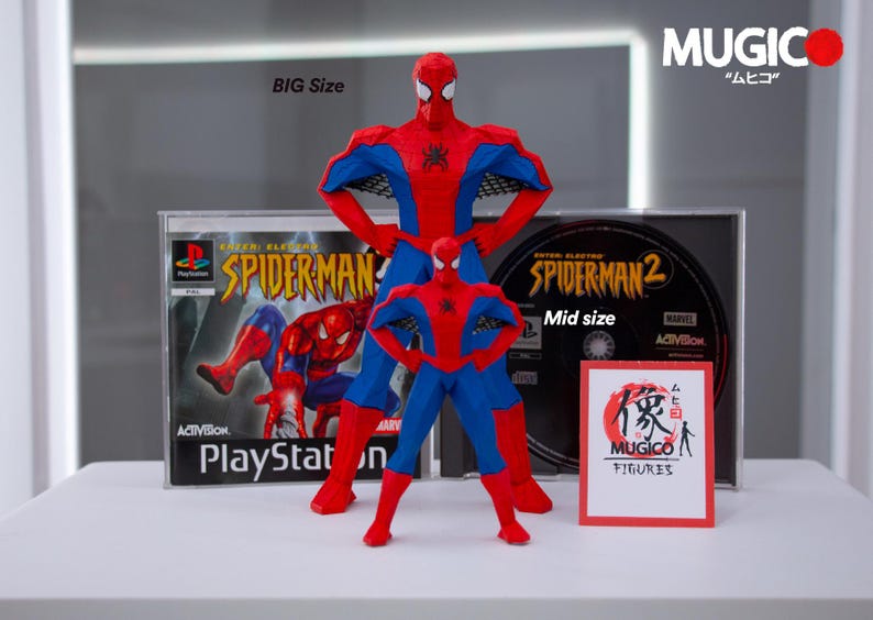 May include: Two Spider-Man action figures, one large and one mid-size, stand in front of PlayStation game cases. The figures are red and blue, with the text "BIG Size" and "Mid size" visible. A small sign reads "MUGICO FIGURES."
