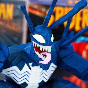 May include: A blue Venom action figure with a white spider symbol on the chest. The figure has a detailed design with sharp teeth, a pink tongue, and white eyes. The figure has multiple antennae.