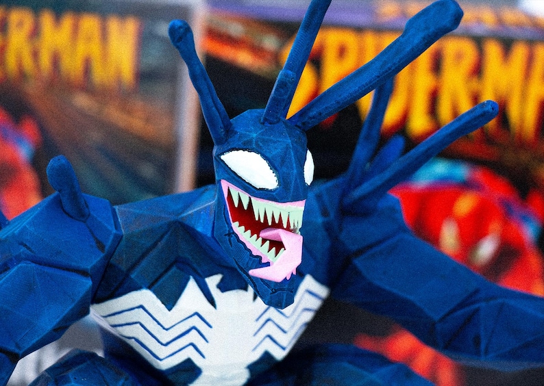 May include: A blue Venom action figure with a white spider symbol on the chest. The figure has a detailed design with sharp teeth, a pink tongue, and white eyes. The figure has multiple antennae.