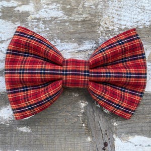 May include: Red and black plaid bow tie. The bow tie is made of a soft, woven fabric.