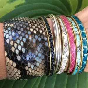 May include: A stack of colourful bracelets with a snakeskin pattern. The bracelets are made of leather and have a variety of colours, including turquoise, pink, and white.