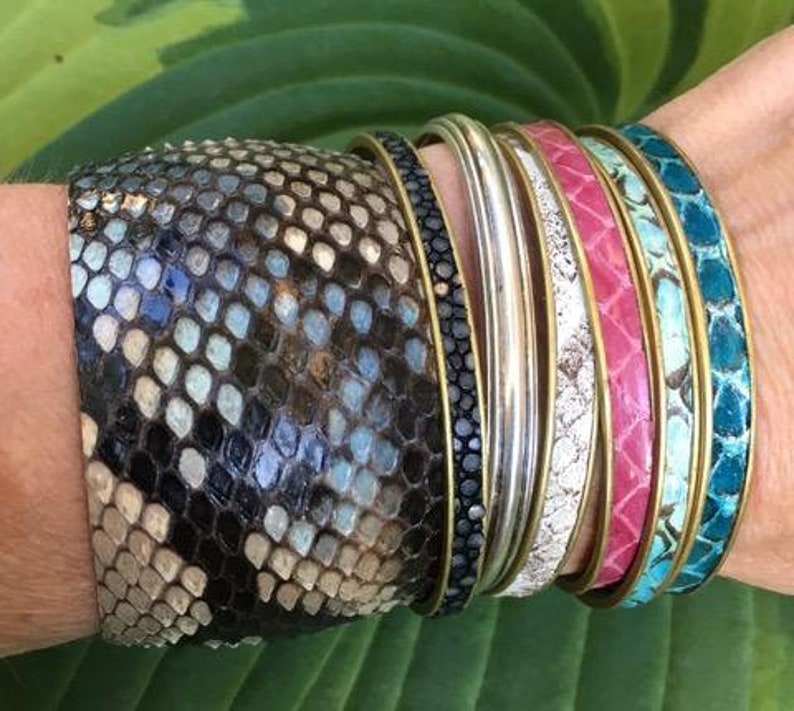 May include: A stack of colourful bracelets with a snakeskin pattern. The bracelets are made of leather and have a variety of colours, including turquoise, pink, and white.