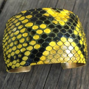 Może przedstawiać: Bransoletka z ż&oacute;łtej i czarnej sk&oacute;ry węża z podstawą z mosiądzu.