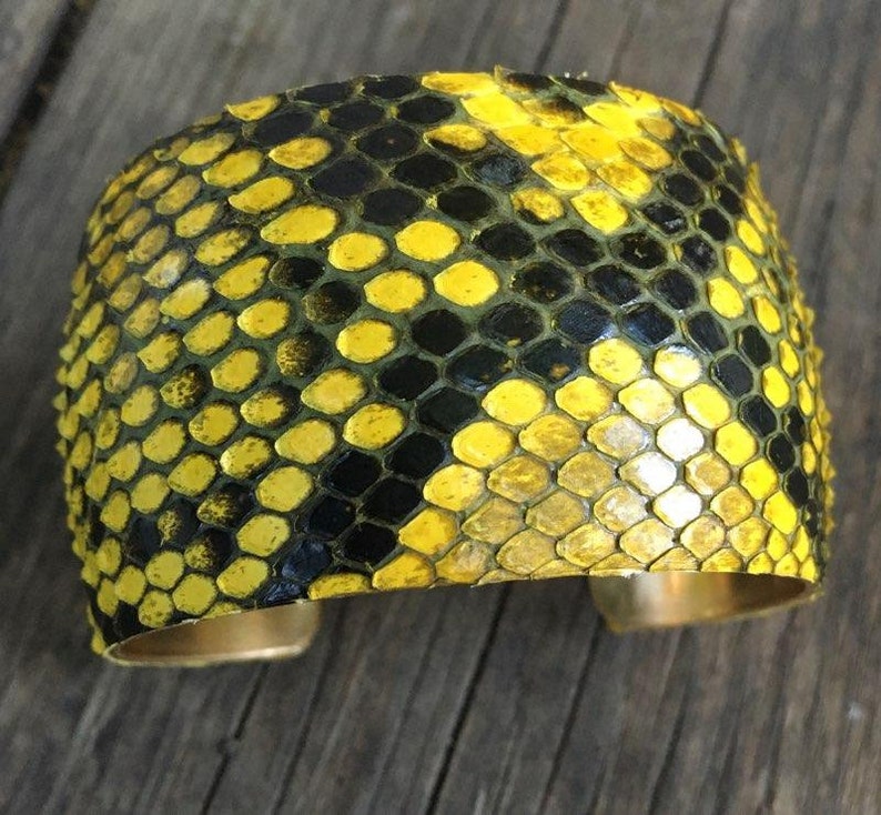 Może przedstawiać: Bransoletka z ż&oacute;łtej i czarnej sk&oacute;ry węża z podstawą z mosiądzu.