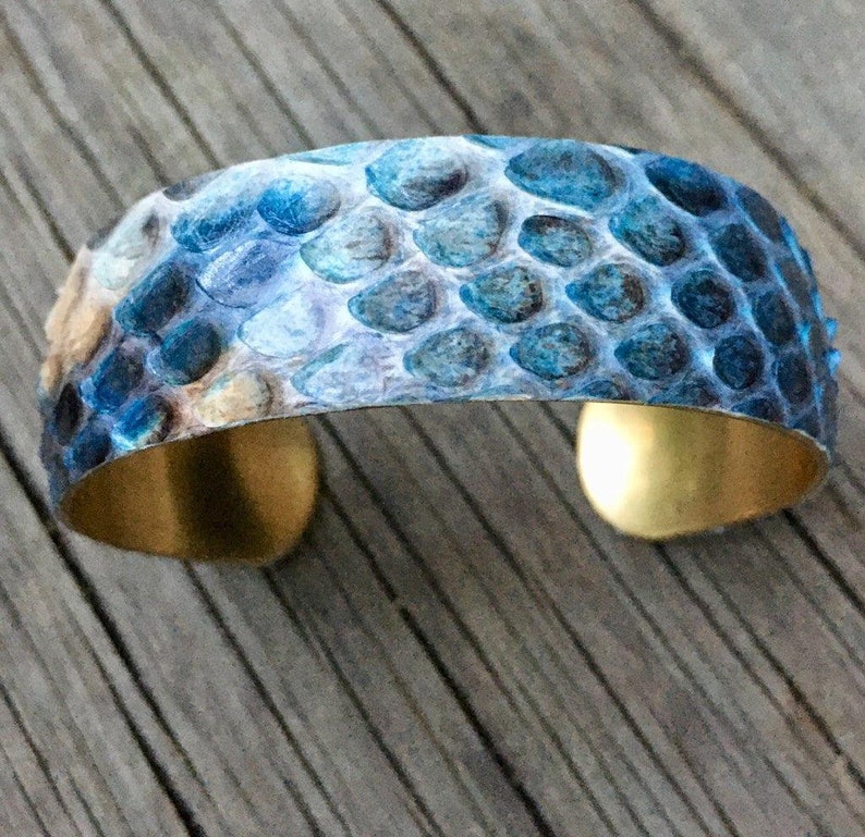 Pu&ograve; includere: Un braccialetto blu e oro con un motivo a pelle di serpente. Il braccialetto &egrave; in metallo e ha una finitura martellata.