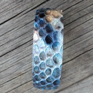 Pu&ograve; includere: Un braccialetto in pelle di serpente blu e marrone con un motivo testurizzato.