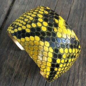 Może przedstawiać: Bransoletka z ż&oacute;łtej i czarnej sk&oacute;ry węża. Bransoletka wykonana jest z prawdziwej sk&oacute;ry węża i ma zapięcie z mosiądzu.