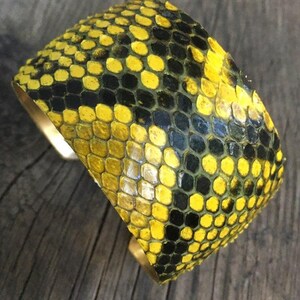 Może przedstawiać: Bransoletka z ż&oacute;łtej i czarnej sk&oacute;ry węża z podstawą z mosiądzu.