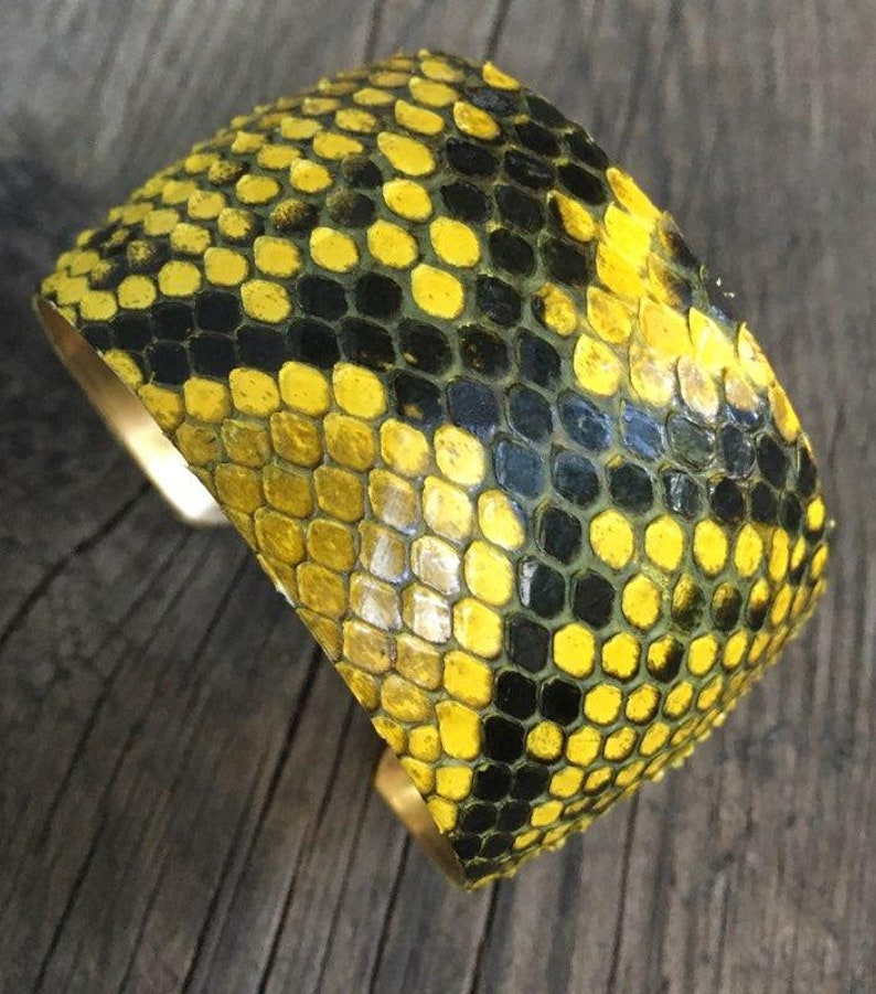 Może przedstawiać: Bransoletka z ż&oacute;łtej i czarnej sk&oacute;ry węża z podstawą z mosiądzu.