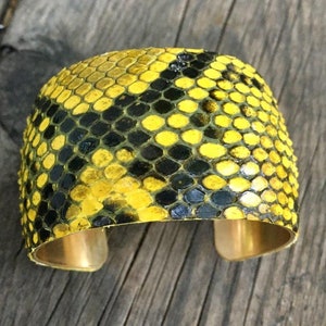 Może przedstawiać: Bransoletka z ż&oacute;łtej i czarnej sk&oacute;ry węża z złotym metalowym paskiem.