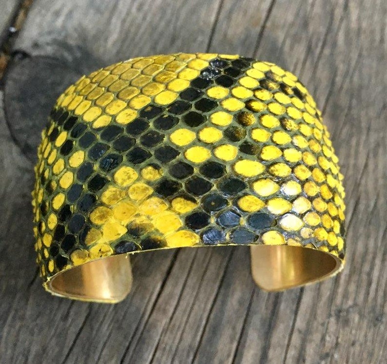 Może przedstawiać: Bransoletka z ż&oacute;łtej i czarnej sk&oacute;ry węża z złotym metalowym paskiem.