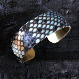 Könnte beinhalten: Ein blaues und schwarzes Schlangenleder-Armband mit Messingbasis.