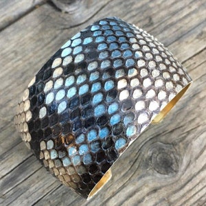 May include: A wide, cuff-style bracelet made of black and blue snakeskin with a brass backing.