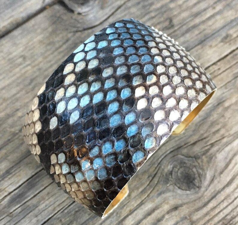 May include: A wide, cuff-style bracelet made of black and blue snakeskin with a brass backing.